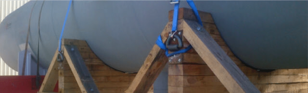 Trincaje de cargas con cinchas y anclajes para asegurar depósito cilíndrico sobre soporte de madera